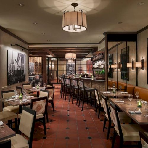 The image shows an elegant restaurant interior with neatly set tables, upscale decor, and warm lighting, creating a cozy dining atmosphere.