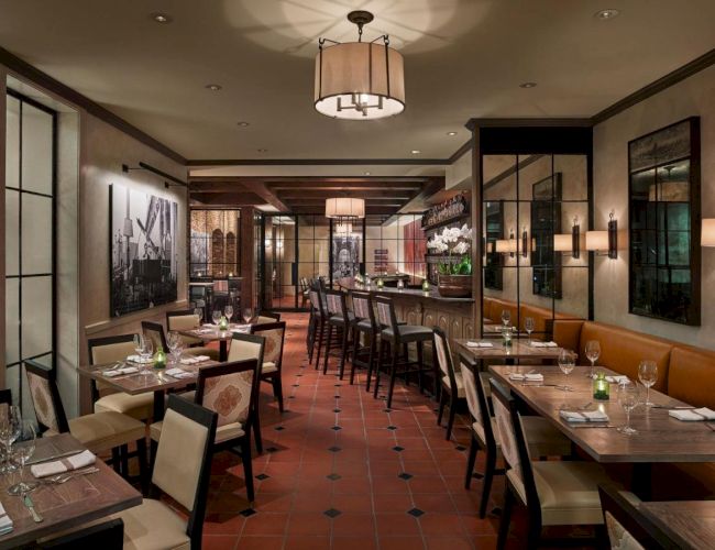 The image shows an elegant restaurant interior with neatly set tables, upscale decor, and warm lighting, creating a cozy dining atmosphere.