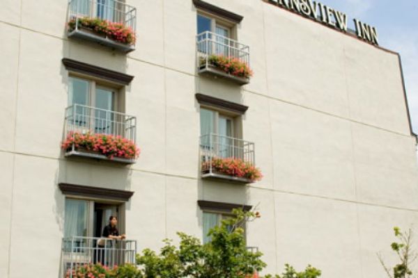 A beige building with balconies and flowers, titled "RIVERVIEW INN," near a large bridge under a blue sky.