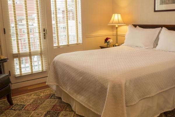 A cozy bedroom with a double bed, white bedding, armchair, table lamp, and window with shutters, creating a warm ambiance.