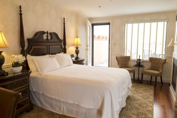 A cozy bedroom with a double bed, lamps on bedside tables, chairs by the window, a dresser, and soft lighting.