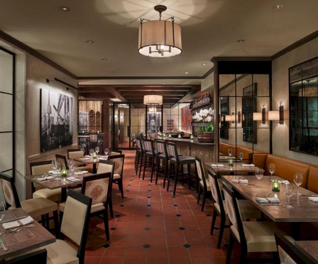 A cozy restaurant interior with tables set for dining, featuring warm lighting, wall decorations, and a bar area in the background.