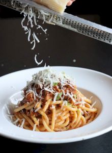 Pasta dish being topped with freshly grated cheese.