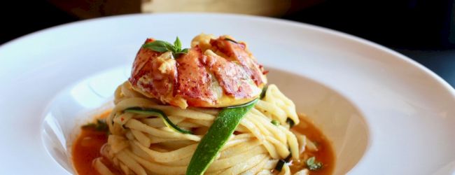 A plate of pasta topped with lobster and garnished with herbs, served in a rich sauce.