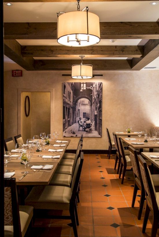 An elegant restaurant interior with wooden beams, set tables, and a large black-and-white photo on the wall, viewed through glass doors.