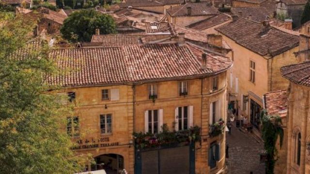 Aerial view of a charming European town with rustic buildings, red-tiled roofs, and cobblestone streets, surrounded by lush greenery.