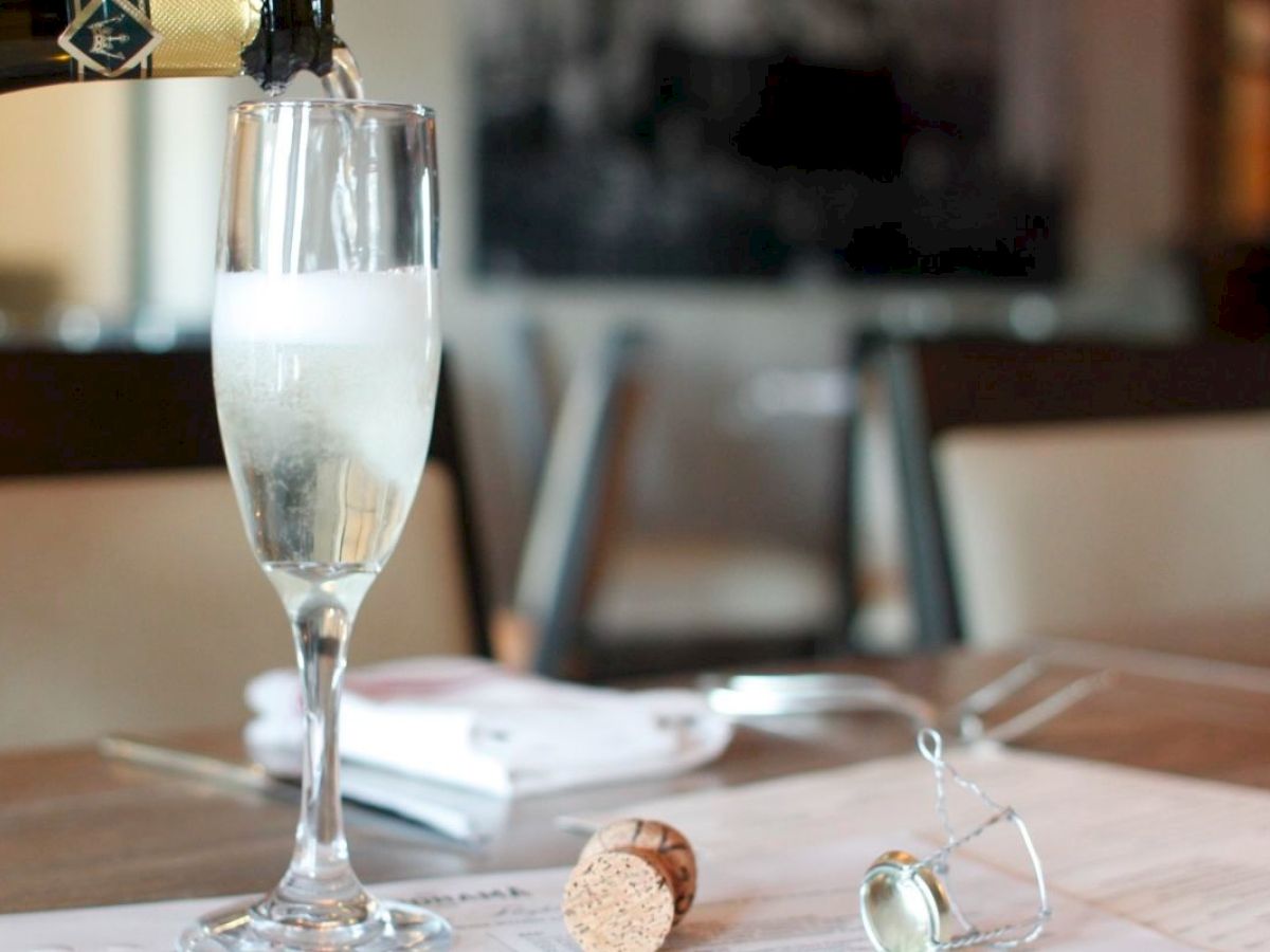 A glass of champagne being poured, with a cork and cage on the table in a dining setting.