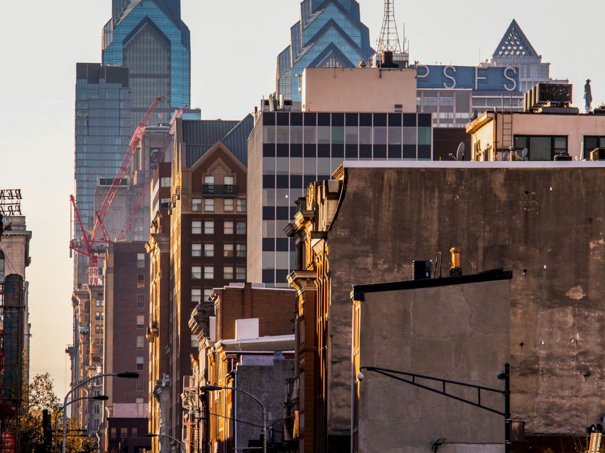 A city street view with cars, buildings in the foreground, and skyscrapers, including two with unique geometric designs, in the background.